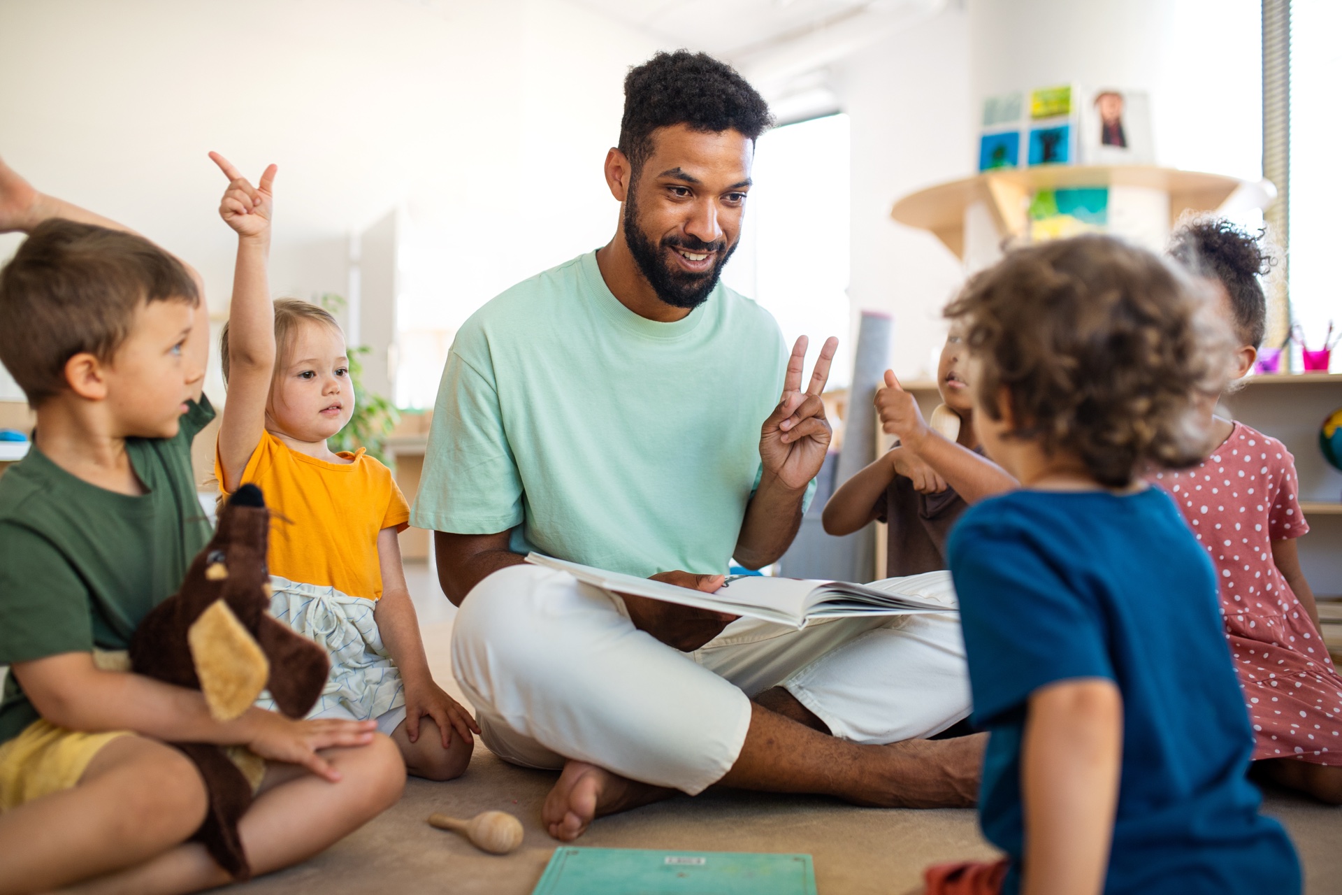 Professionele kinderopvang begeleider leest voor aan diverse groep jonge kinderen in modern kinderdagverblijf met educatief speelgoed